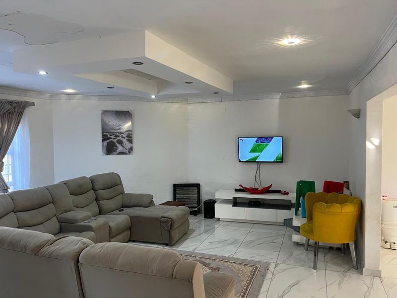 Spacious living room featuring marble-look floor tiles, a recessed ceiling with downlights, and coving detail. Note visible ceiling water staining.