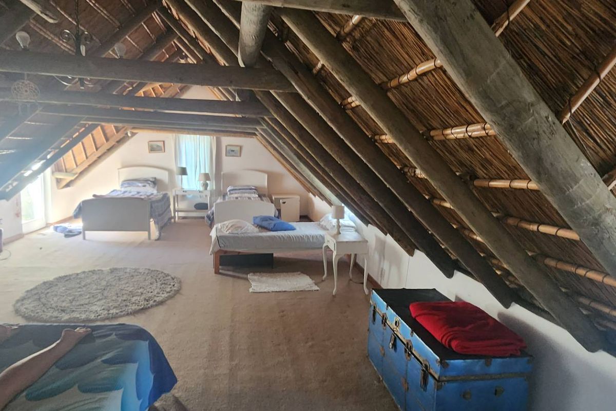 Spacious attic-style bedroom featuring exposed timber rafters and traditional thatch roofing, providing a rustic and open living environment.