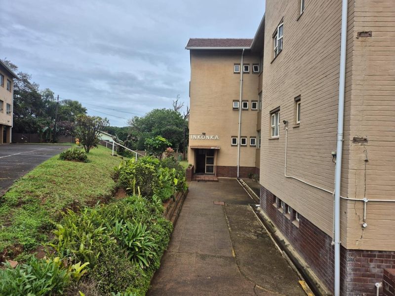 Exterior view of the Inkonka apartment building featuring a brick facade, paved walkway, and surrounding landscaped garden area.