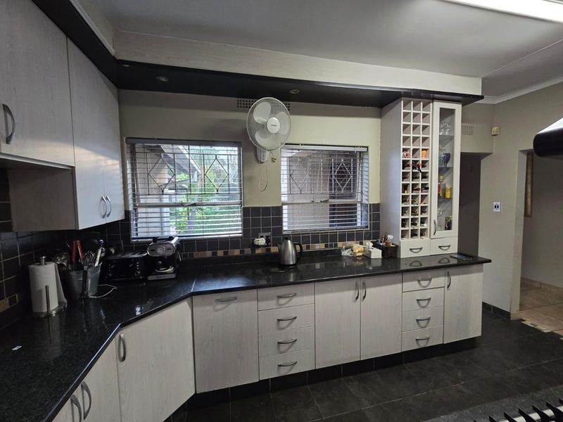 A functional kitchen featuring granite countertops, ample built-in cabinetry with a wine rack, tiled backsplash, and tiled flooring.
