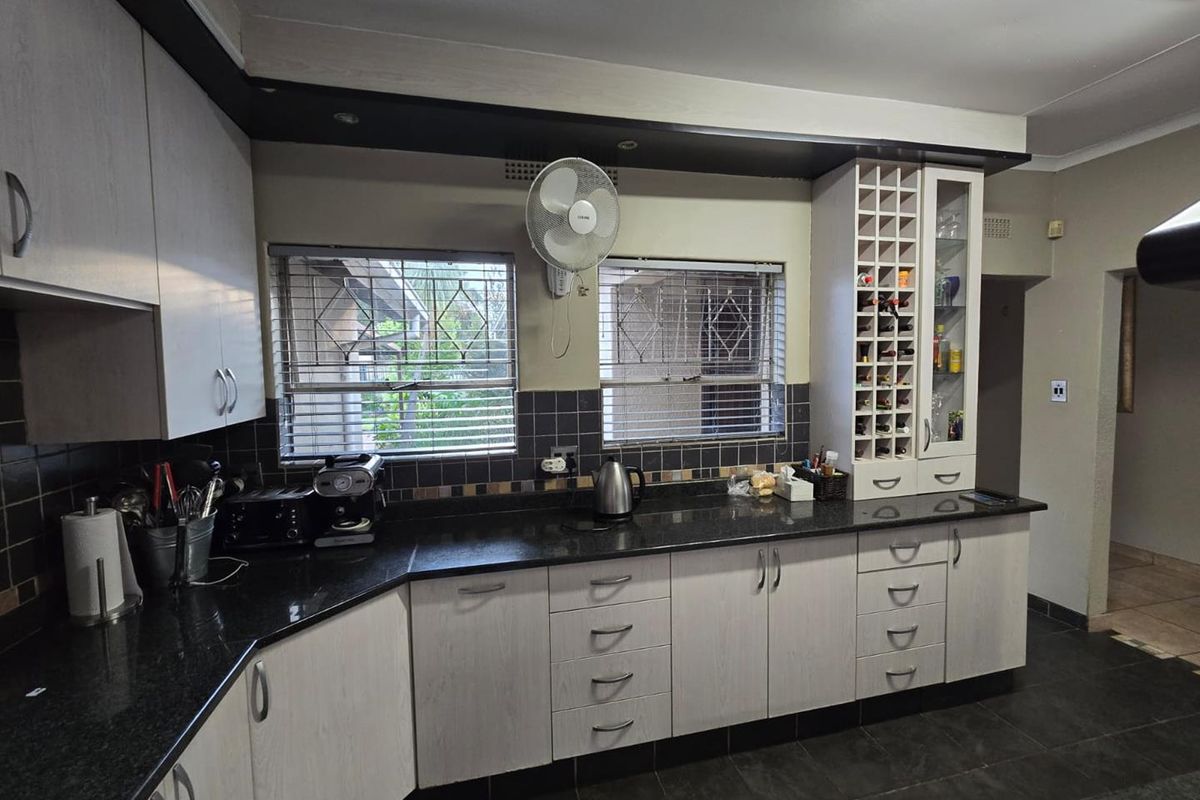 A functional kitchen featuring granite countertops, ample built-in cabinetry with a wine rack, tiled backsplash, and tiled flooring.