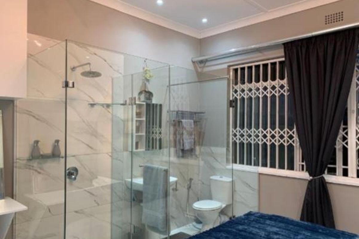 Modern bathroom featuring a glass-enclosed shower with a rain shower head, marble-look wall tiles, a wall-mounted basin, and a toilet.
