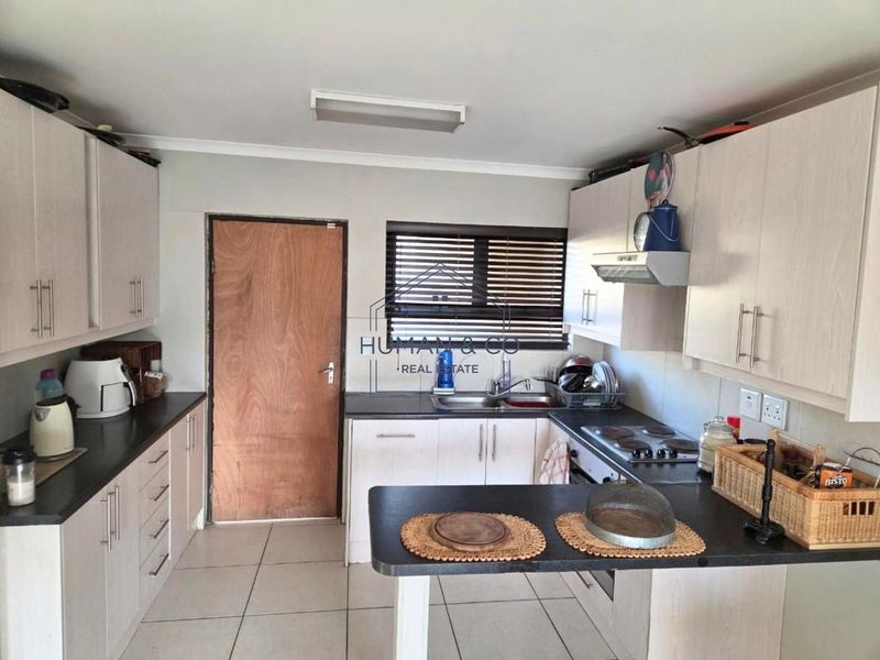 A functional kitchen featuring light-toned built-in cabinetry, dark laminate countertops, an electric hob with extractor fan, and tiled flooring.