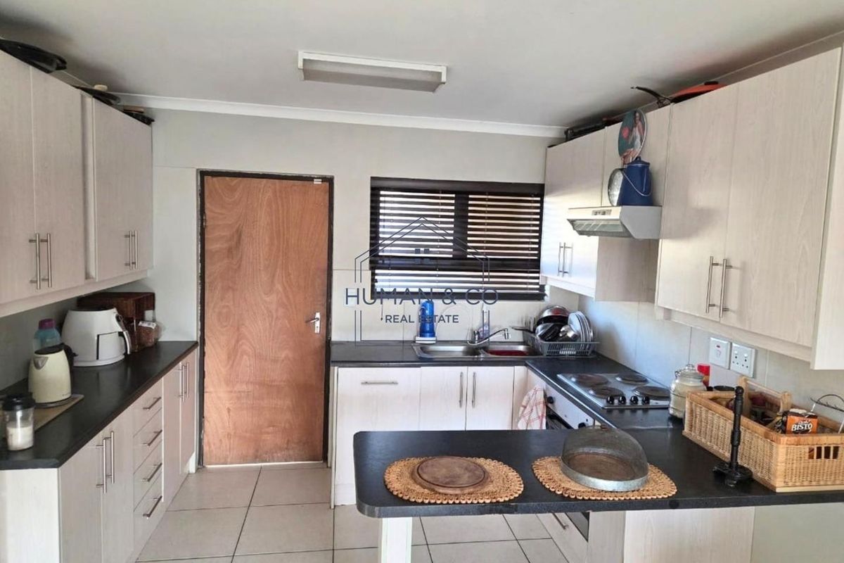 A functional kitchen featuring light-toned built-in cabinetry, dark laminate countertops, an electric hob with extractor fan, and tiled flooring.