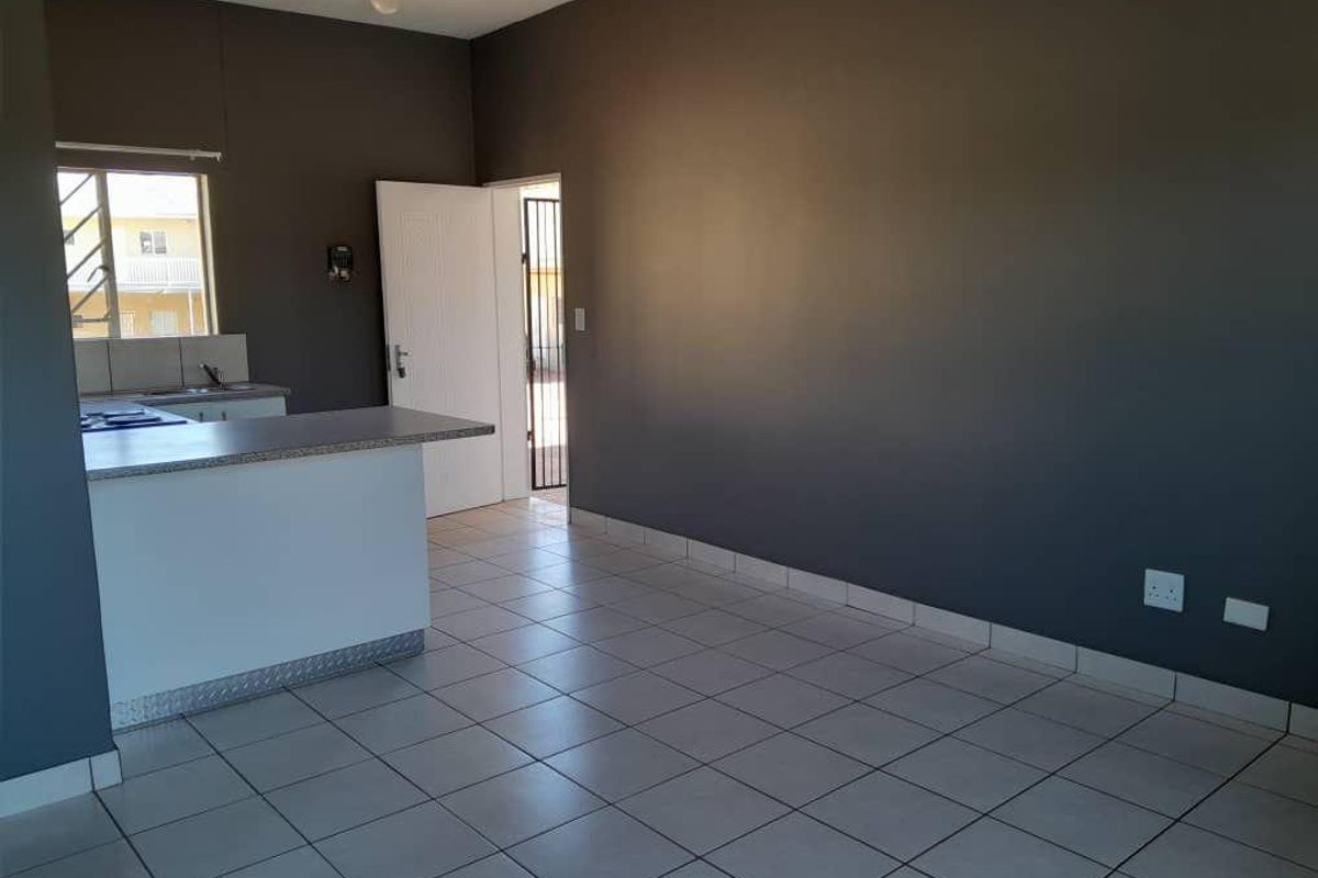 An open-plan living and kitchen area featuring tiled flooring, a breakfast bar, and direct access to an exterior entrance.