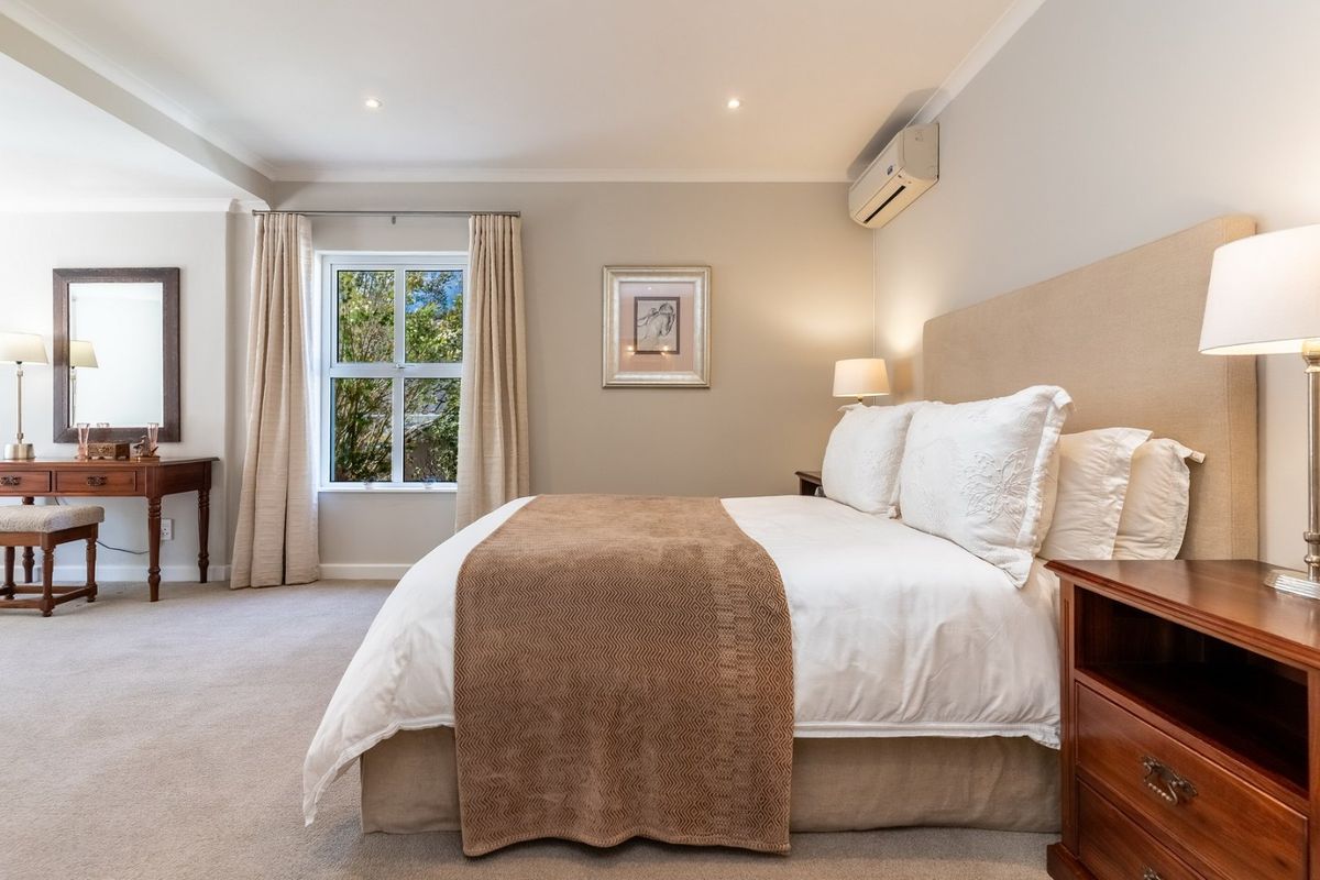 A well-maintained bedroom featuring neutral wall tones, carpeted flooring, recessed lighting, and a wall-mounted air conditioning unit.