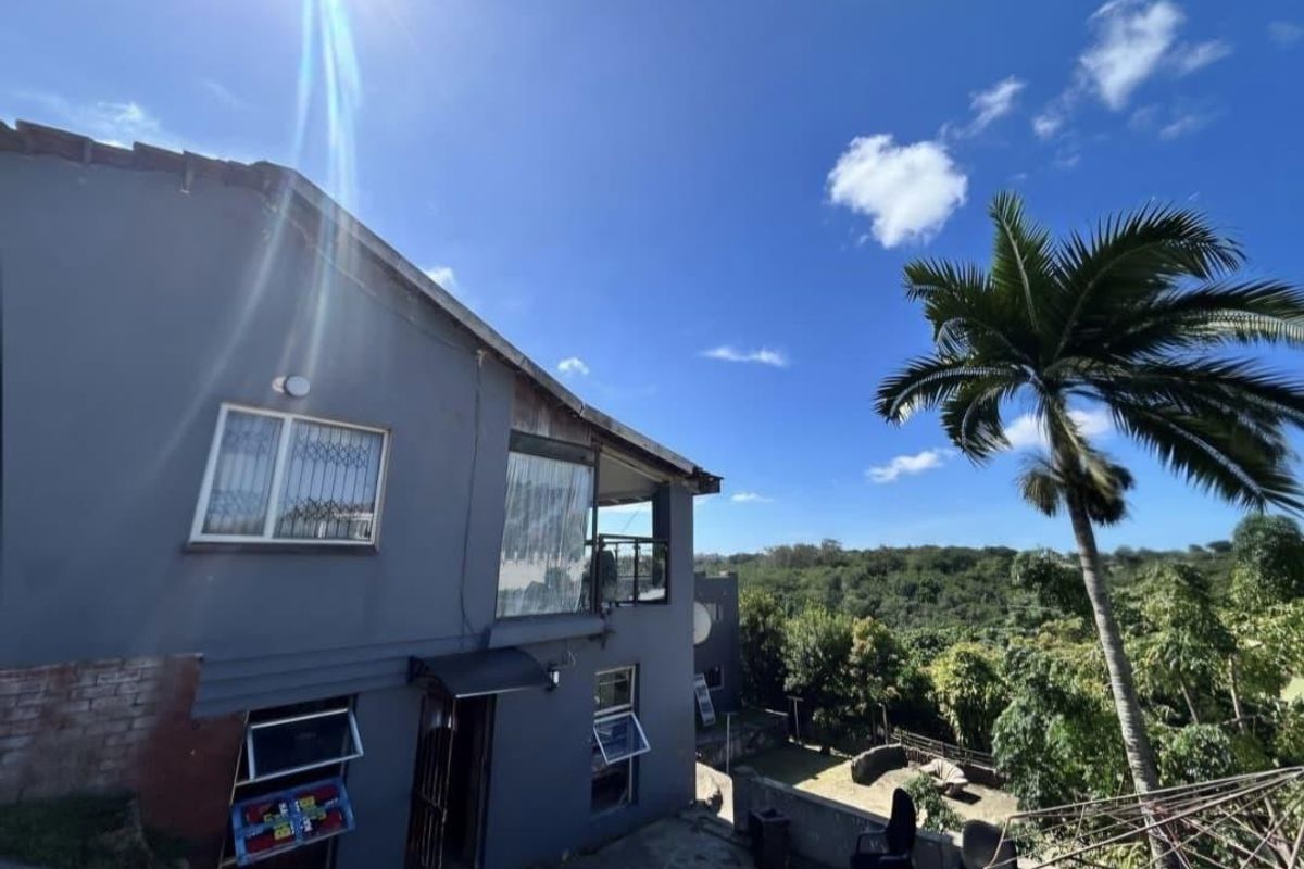 Rear exterior view of a multi-level house featuring a stone patio, security bars on windows, and a scenic view of the surrounding landscape.