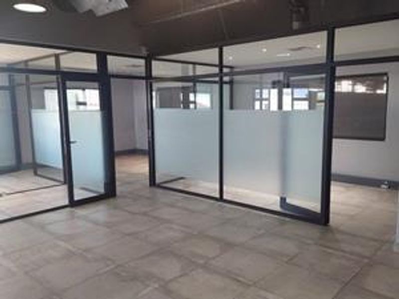 Modern industrial office space featuring glass partition walls, tiled flooring, and recessed lighting, providing a clean and professional environment.