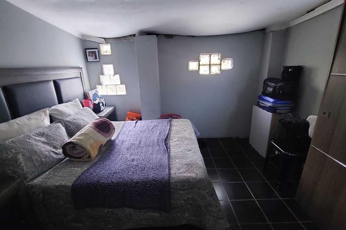A bedroom featuring dark tiled flooring, glass block windows for natural light, and a built-in wardrobe, requiring some ceiling repairs.