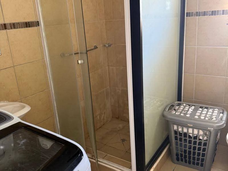 A functional bathroom featuring a glass-enclosed shower with tiled walls and flooring, showing signs of wear and requiring maintenance.