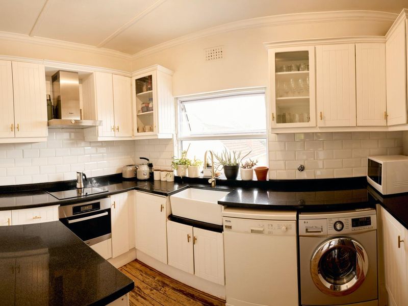 A well-appointed kitchen featuring white shaker-style cabinetry, black granite countertops, a classic farmhouse sink, and subway tile backsplash with integrated stainless steel appliances.