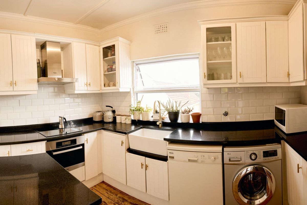 A well-appointed kitchen featuring white shaker-style cabinetry, black granite countertops, a classic farmhouse sink, and subway tile backsplash with integrated stainless steel appliances.