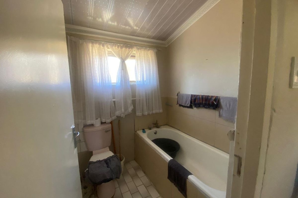 A compact bathroom featuring a standard bathtub, toilet, and tiled flooring, requiring modernization to update the dated finishes and fixtures.