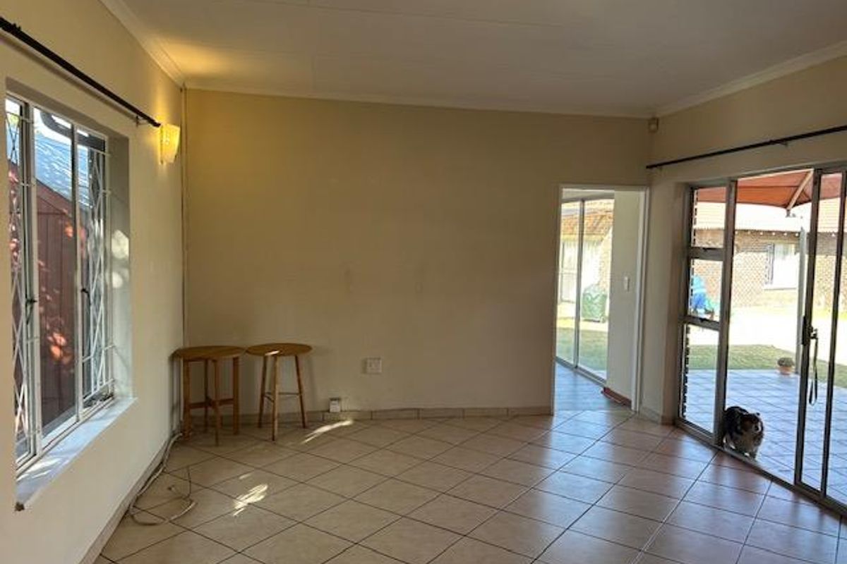 A bright, empty living room featuring tiled flooring, large sliding glass doors leading to the patio, and security bars on the windows.