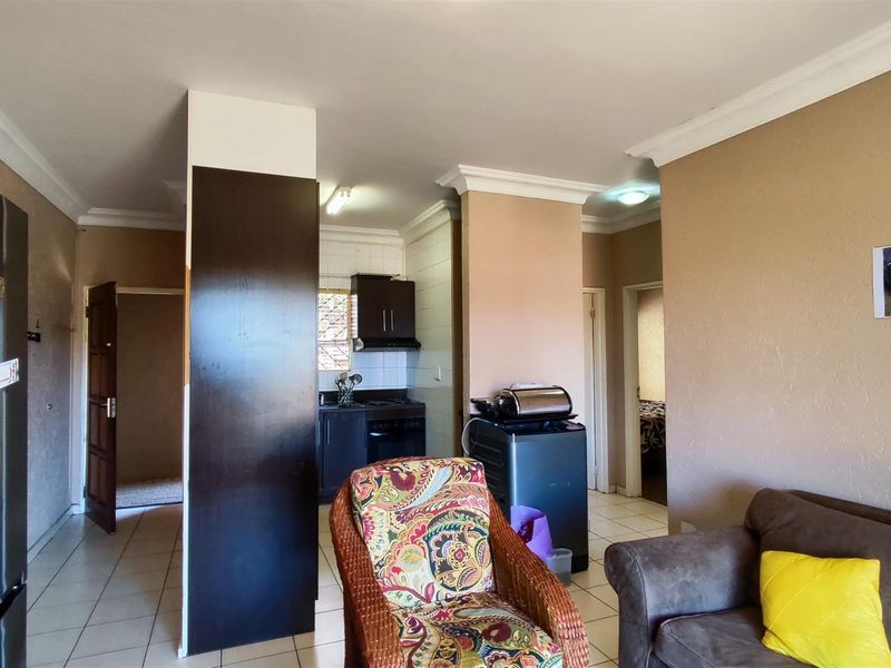 Open-plan living area featuring tiled flooring, cornicing, and a compact kitchen space with built-in cabinetry and an extractor fan.