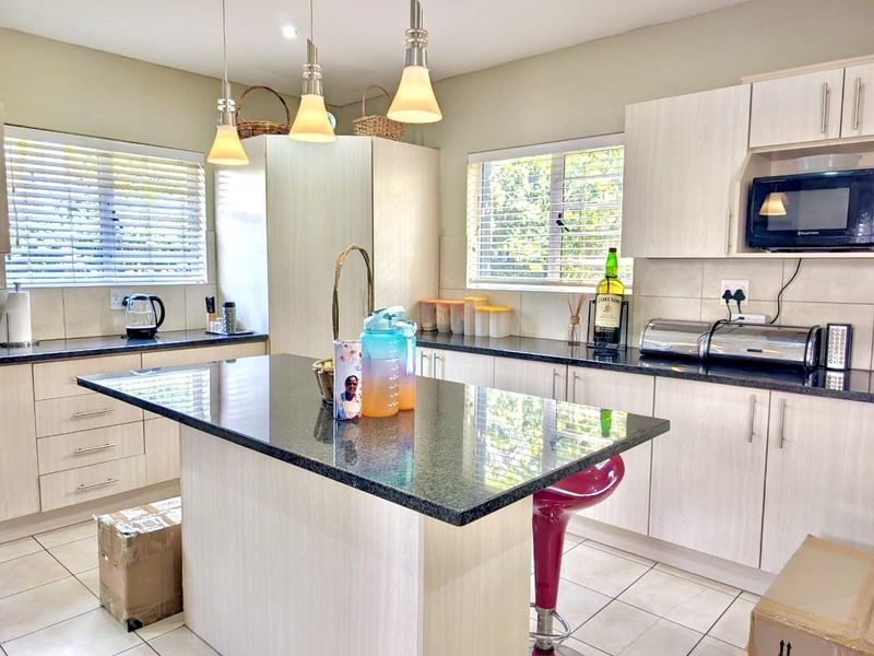 A well-maintained kitchen featuring light wood-finish cabinetry, dark granite countertops, a central island, and modern pendant lighting.