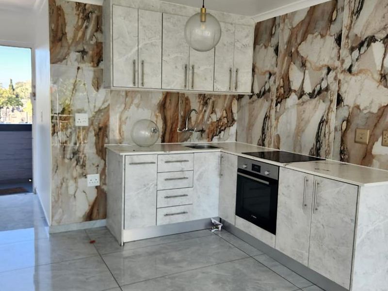 Modern kitchen featuring marble-effect wall cladding, sleek built-in cabinetry, integrated oven, electric hob, and polished porcelain floor tiles.
