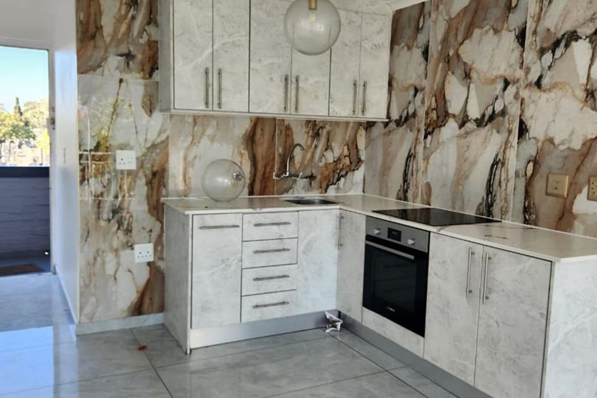 Modern kitchen featuring marble-effect wall cladding, sleek built-in cabinetry, integrated oven, electric hob, and polished porcelain floor tiles.