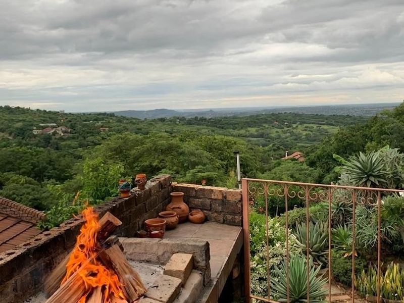 An elevated outdoor patio featuring a built-in brick braai, tiled flooring, and a wrought iron railing with expansive views of the surrounding landscape.