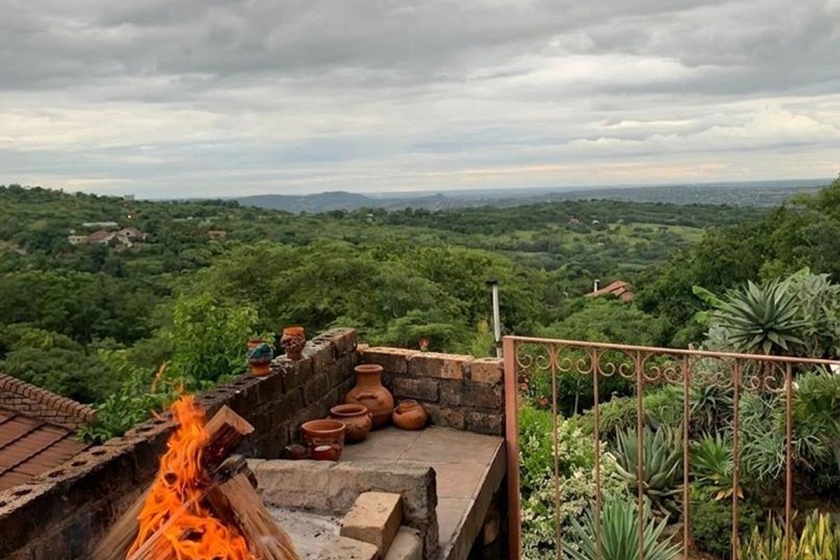 An elevated outdoor patio featuring a built-in brick braai, tiled flooring, and a wrought iron railing with expansive views of the surrounding landscape.