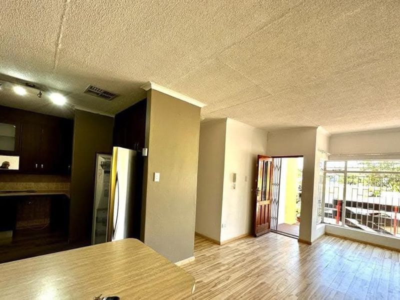 Open plan living area featuring laminate flooring, track lighting, and an integrated kitchen space with built-in cabinetry, leading to an exterior entrance.