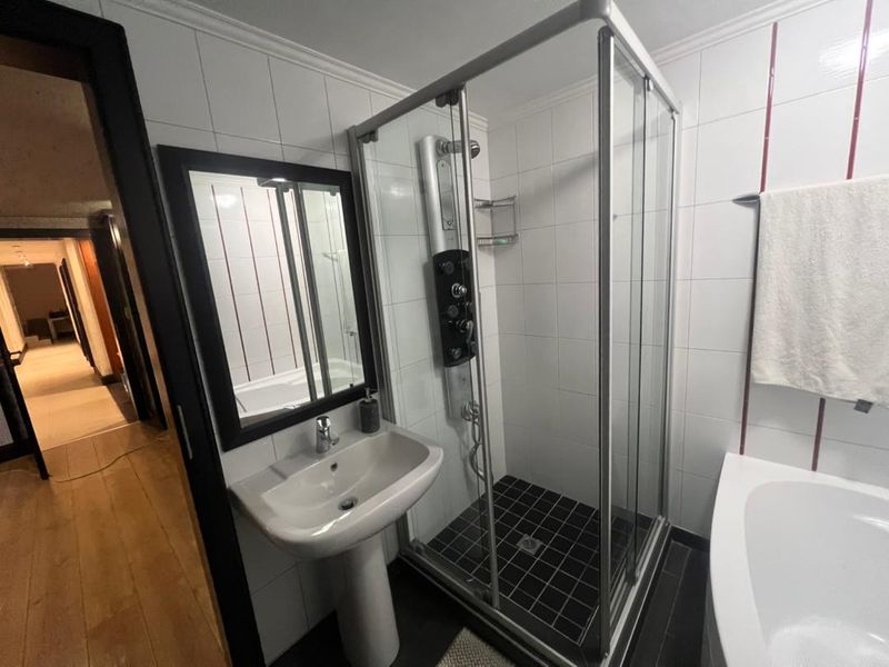 A functional bathroom featuring a pedestal basin, a separate shower enclosure with a modern shower panel, and a bathtub with white wall tiling.
