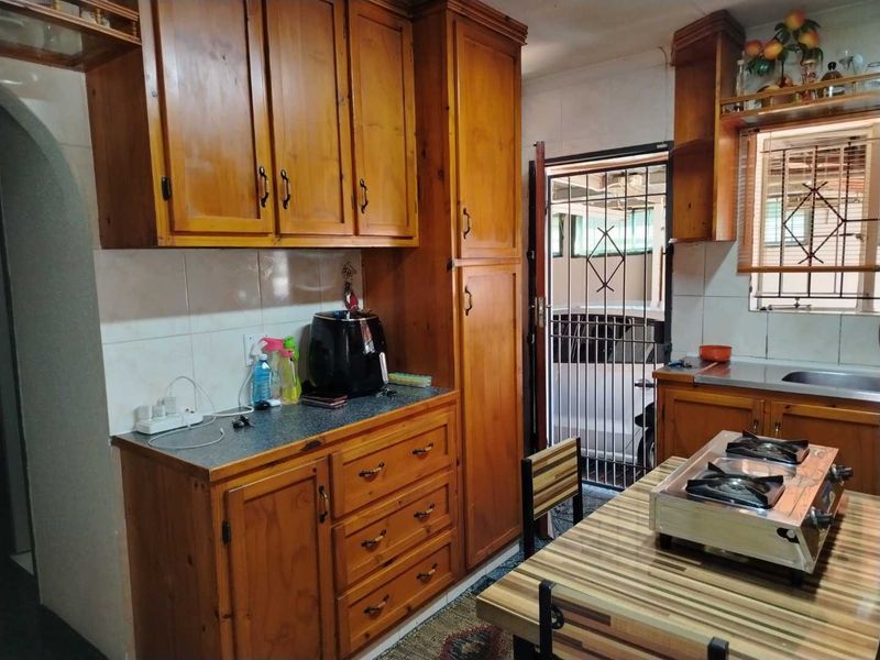 A functional kitchen featuring traditional wooden cabinetry, laminate countertops, a tiled backsplash, and direct access to an exterior security gate.