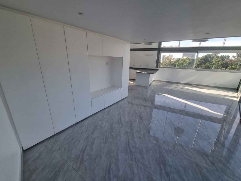 Spacious open-plan living area featuring sleek built-in cabinetry, polished marble-look floor tiles, and large windows offering abundant natural light and exterior views.