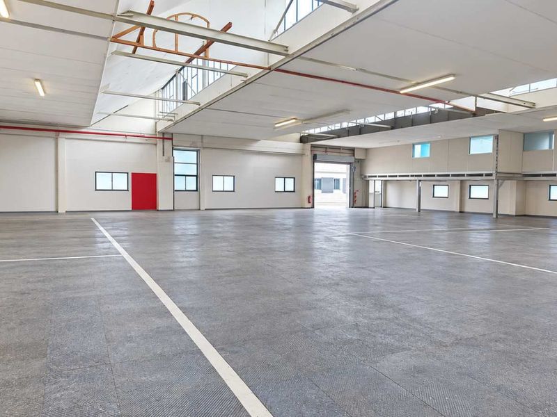 Spacious industrial warehouse featuring high ceilings, concrete flooring, ample natural light through skylights, and a large roller shutter door for easy access.