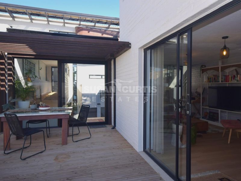 A covered timber deck patio featuring a pergola and large sliding glass doors providing seamless indoor-outdoor flow to the living area.