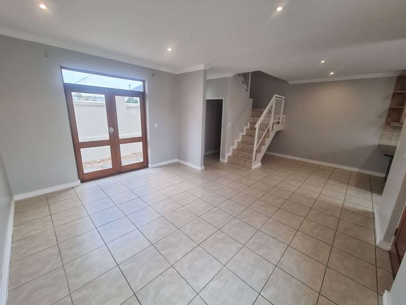 Spacious open-plan living area featuring neutral tiled flooring, recessed lighting, and a staircase leading to the upper level with direct access to the exterior.