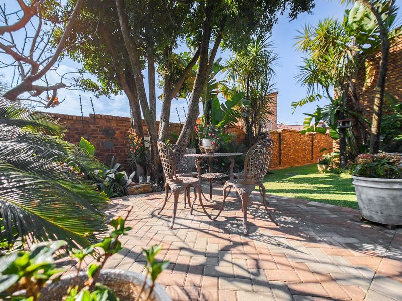 A well-maintained garden featuring brick paving, mature trees, and a secure brick boundary wall with electric fencing.