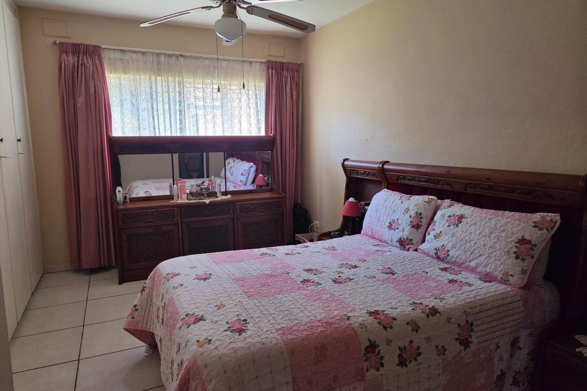 A bedroom featuring tiled flooring, a ceiling fan, and built-in cupboards, offering a functional space with neutral wall finishes.