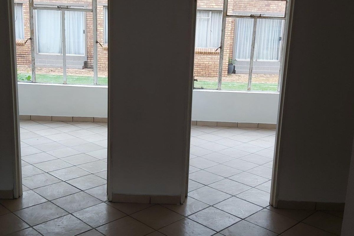 A view from an interior space looking out through two doorways into a tiled patio or sunroom area with large windows.