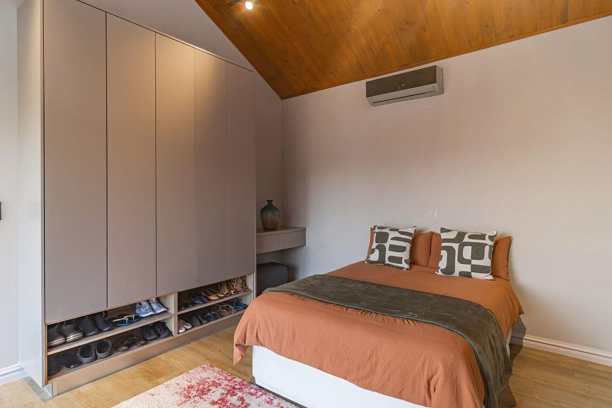 A well-maintained bedroom featuring built-in floor-to-ceiling cabinetry, a vaulted timber-clad ceiling, and a wall-mounted air conditioning unit.