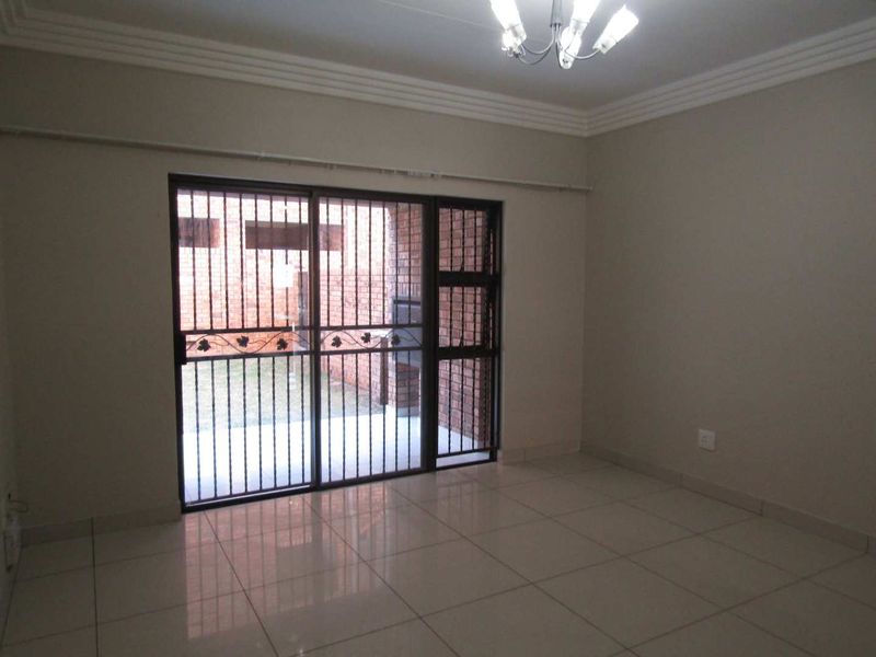 An empty living room featuring tiled flooring, crown molding, and a sliding glass door with an integrated security gate leading to an outdoor area.
