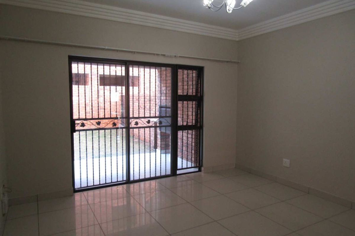 An empty living room featuring tiled flooring, crown molding, and a sliding glass door with an integrated security gate leading to an outdoor area.