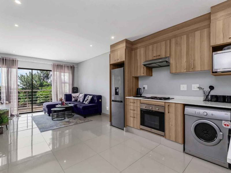 Modern open-plan living area featuring a sleek kitchen with built-in appliances, stone countertops, and seamless flow to a private balcony.