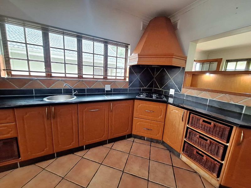 A functional kitchen featuring wooden cabinetry, granite countertops, a gas hob with an extractor hood, and tiled flooring.