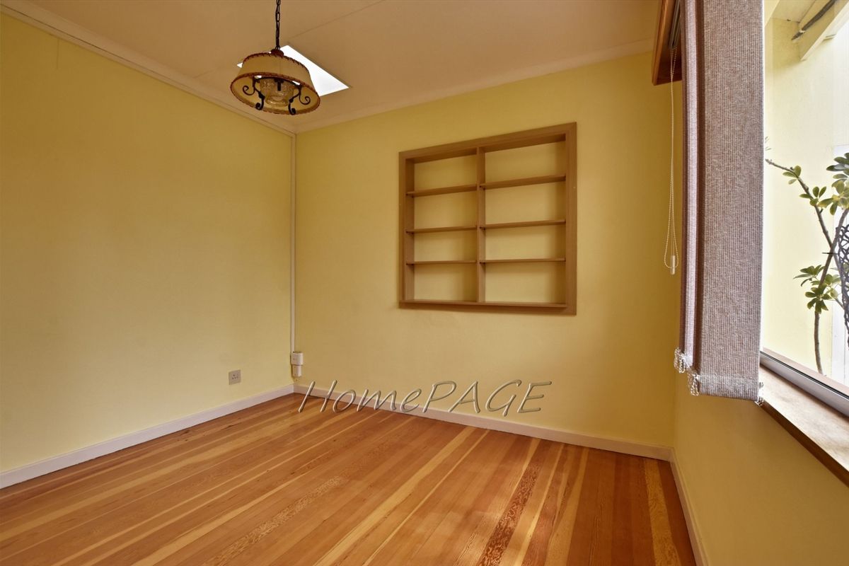 A bright bedroom featuring polished timber flooring, built-in wall shelving, and a pendant light fixture.