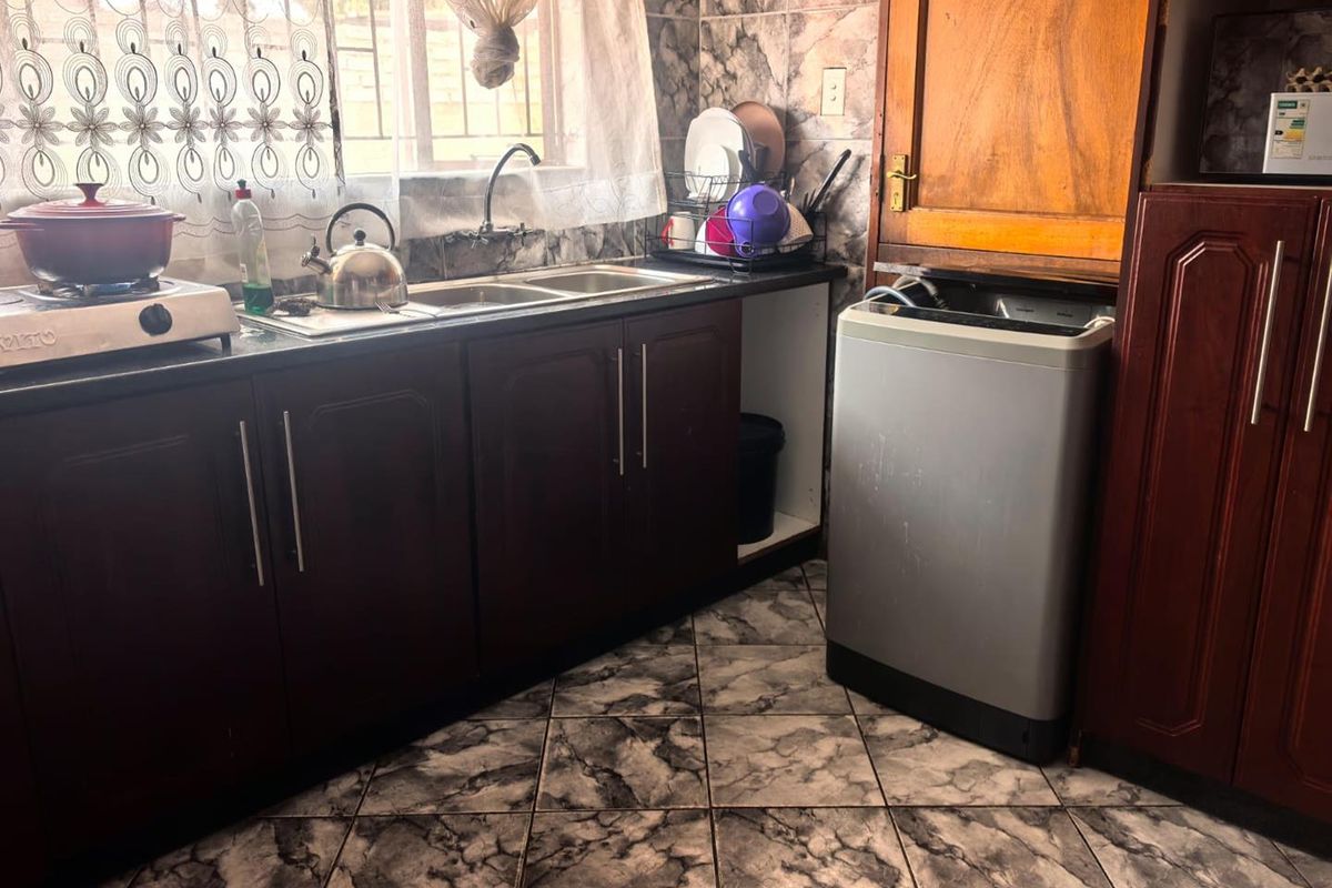 A functional kitchen featuring dark wood cabinetry, a double basin sink, and tiled finishes, providing a practical workspace for daily meal preparation.