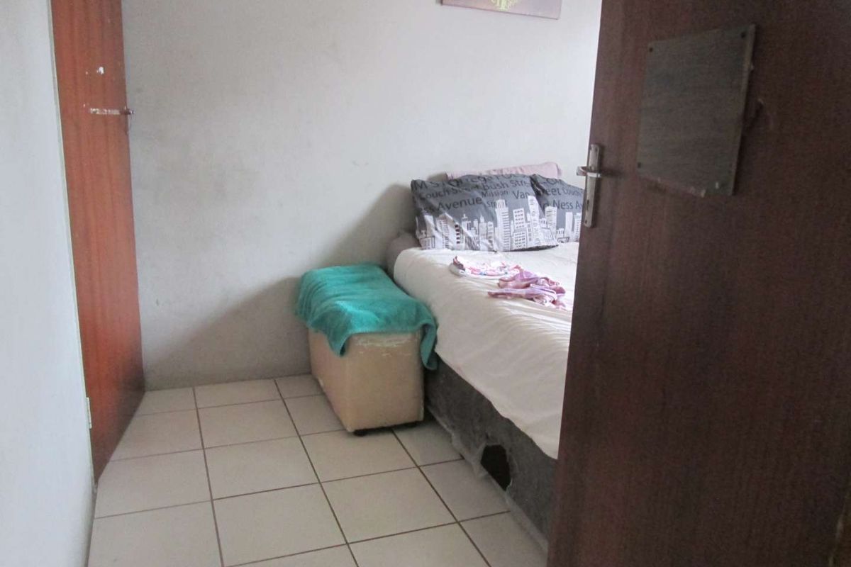 A compact bedroom featuring tiled flooring and a wooden door, providing a functional sleeping space within the apartment.