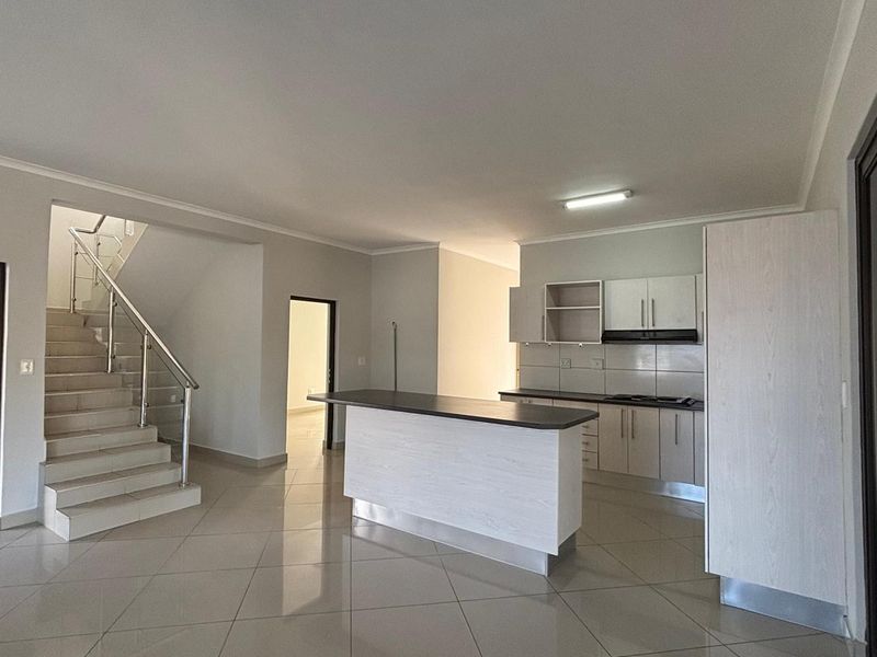 Spacious open-plan kitchen and living area featuring modern cabinetry, a central island, and a staircase with a stainless steel balustrade.