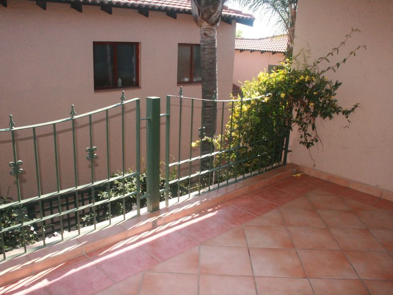 A private balcony featuring terracotta tiled flooring and a decorative wrought iron railing, overlooking the surrounding residential complex.