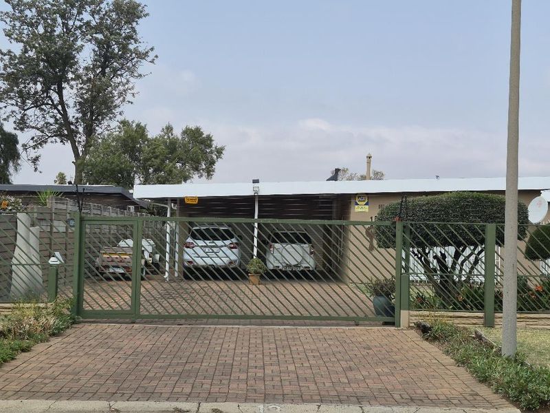 Front view of the property featuring a paved driveway, secure metal gate, and a covered carport area.