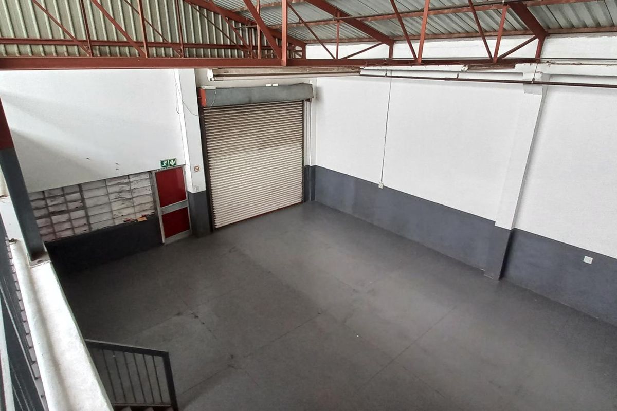 Spacious industrial warehouse unit featuring high ceilings with exposed steel trusses, a large roller shutter door, and durable painted concrete flooring.