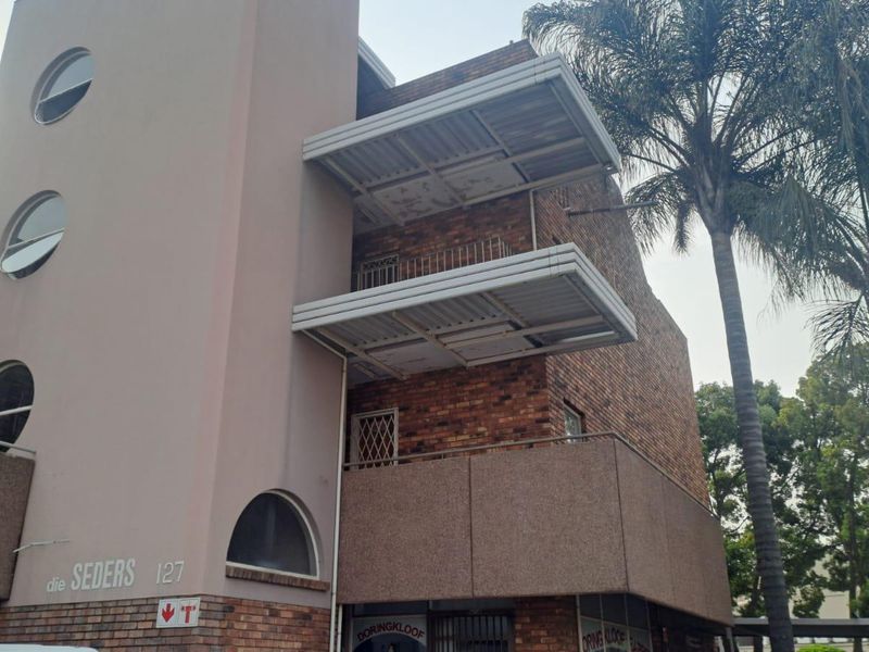 Exterior view of a multi-story apartment building featuring brick masonry, circular windows, and private balconies with metal roof coverings.