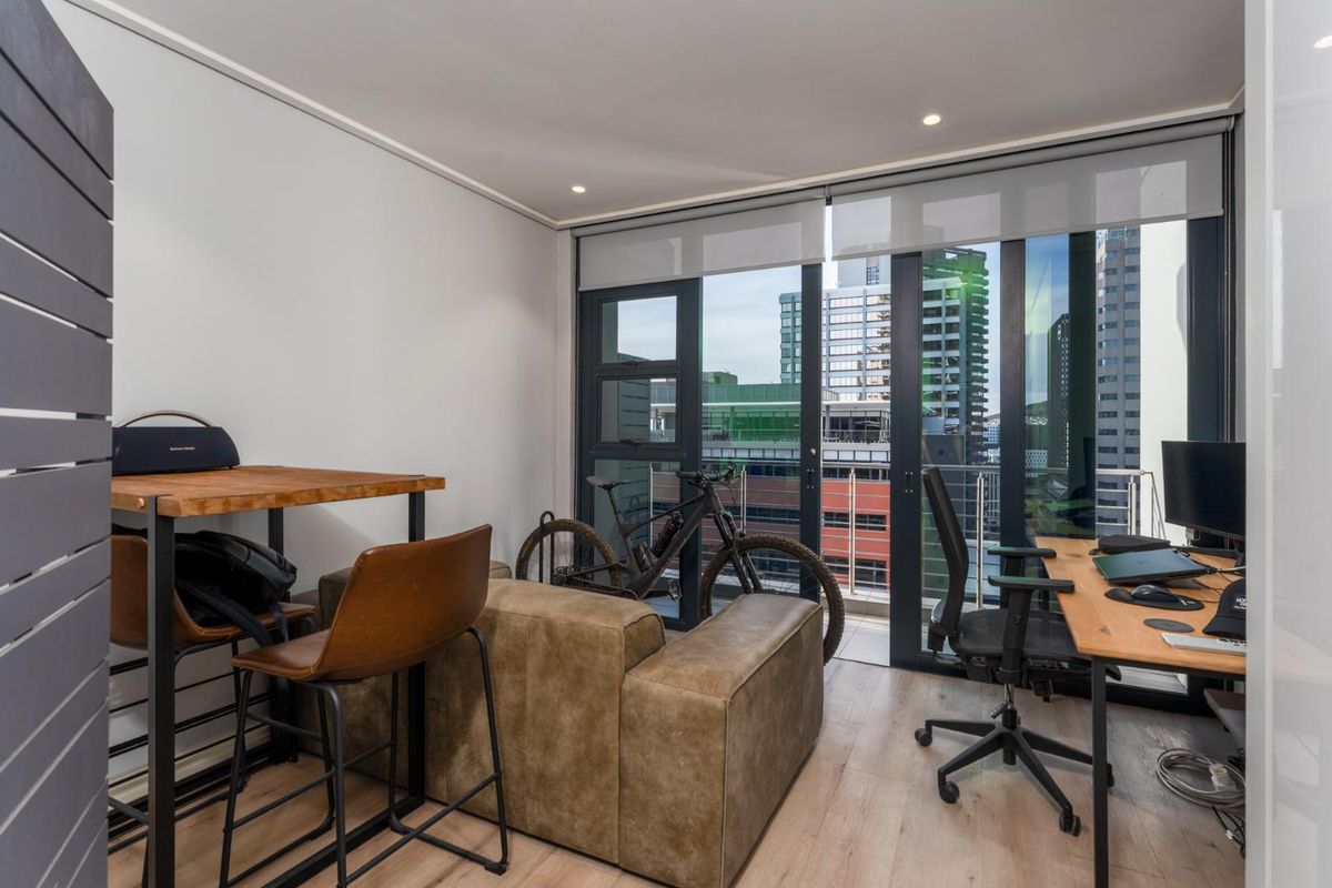 A modern living area featuring laminate flooring, recessed downlights, and large sliding glass doors that open to a balcony with city views.