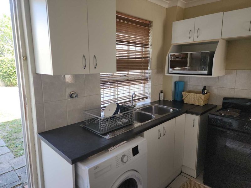 Compact kitchen featuring white cabinetry, dark laminate countertops, double sink, and space for a washing machine, with direct access to the outdoor area.