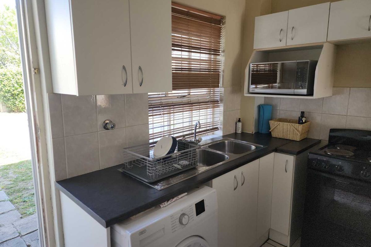 Compact kitchen featuring white cabinetry, dark laminate countertops, double sink, and space for a washing machine, with direct access to the outdoor area.